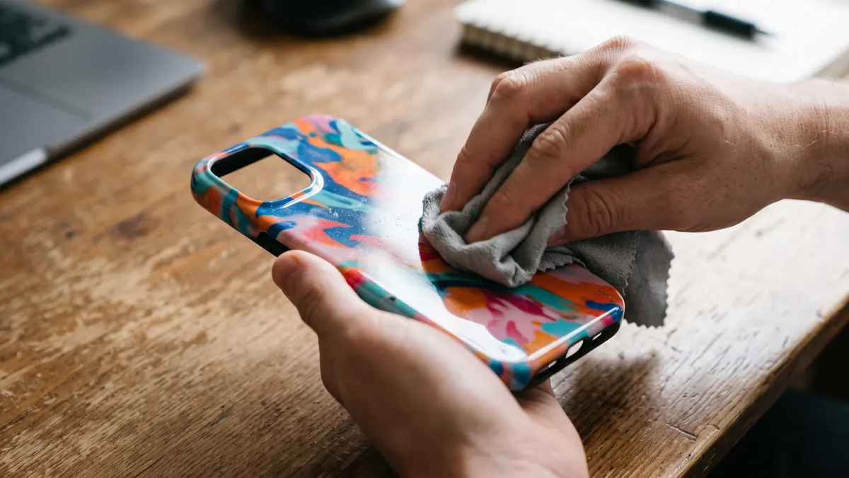 Ilustrasi tangan membersihkan case HP keras bermotif dengan kain microfiber abu-abu
