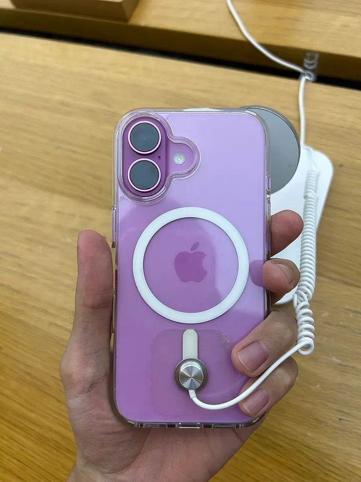 iPhone 16 warna pink terpasang case bening dengan cincin magnet di bagian belakang